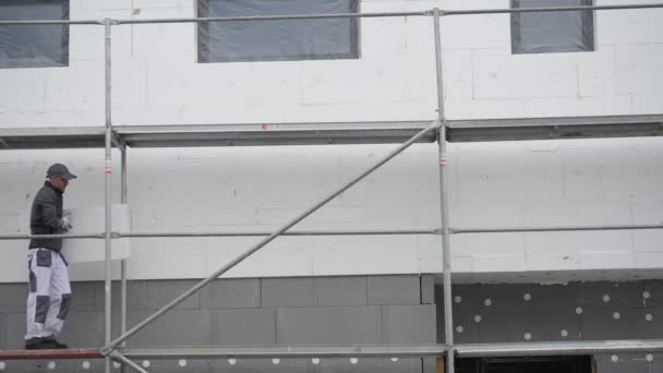 Kaukasische werknemer op een steiger werken met externe gebouw isolatie. - Video