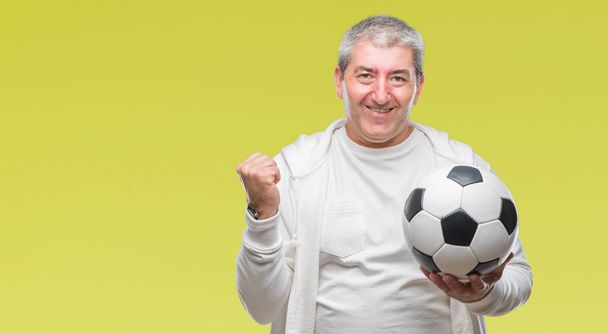 Handsome senior man holding soccer football ball over isolated background screaming proud and celebrating victory and success very excited, cheering emotion - Photo, Image