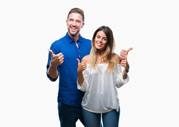 Young couple in love over isolated background success sign doing positive gesture with hand, thumbs up smiling and happy. Looking at the camera with cheerful expression, winner gesture. - Foto, imagen