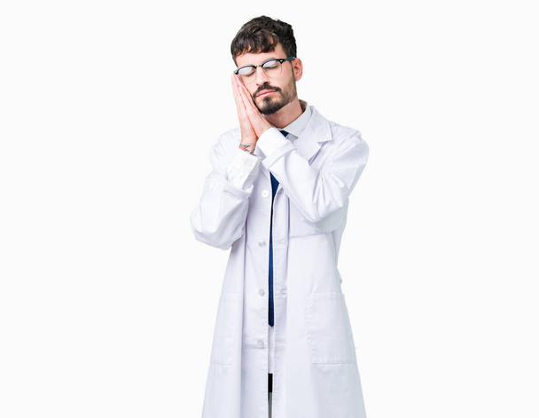 Young professional scientist man wearing white coat over isolated background sleeping tired dreaming and posing with hands together while smiling with closed eyes. - Photo, Image