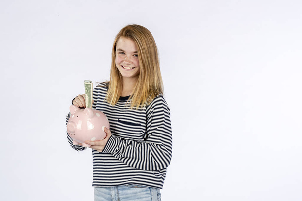 Una hermosa modelo adolescente rubia sosteniendo una alcancía y ahorrando dinero
 - Foto, Imagen