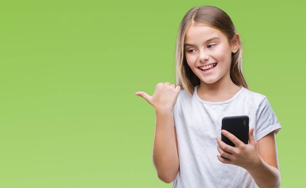 Молодая красивая девушка отправляет сообщения с помощью смартфона на изолированном фоне указывая и показывая с большим пальцем вверх в сторону со счастливым лицом улыбаясь
 - Фото, изображение