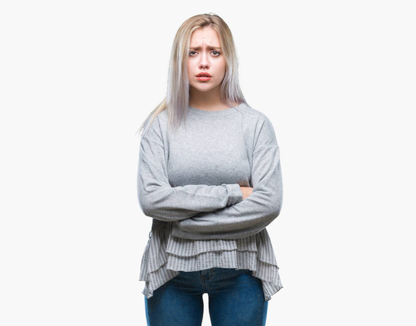 Jonge blonde vrouw over geïsoleerde achtergrond scepticus en nerveus, afkeurende uitdrukking op het gezicht met gekruiste armen. Negatief persoon. - Foto, afbeelding