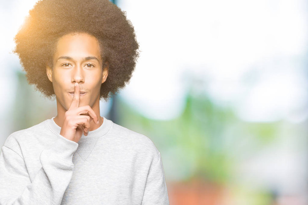 Afrikalı-Amerikalı genç afro saçlı dudaklarında parmak ile sessiz olmanı sportif kazak giyiyor. Sessizlik ve gizli kavramı. - Fotoğraf, Görsel
