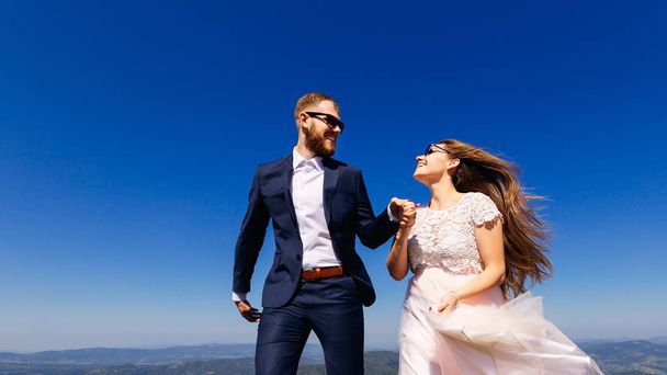 お互いに、自分の顔に笑顔をウェディング ドレスで新婚のクローズ アップは、サングラスです。地平線と雲一つない空に山からの美しい眺め - 写真・画像