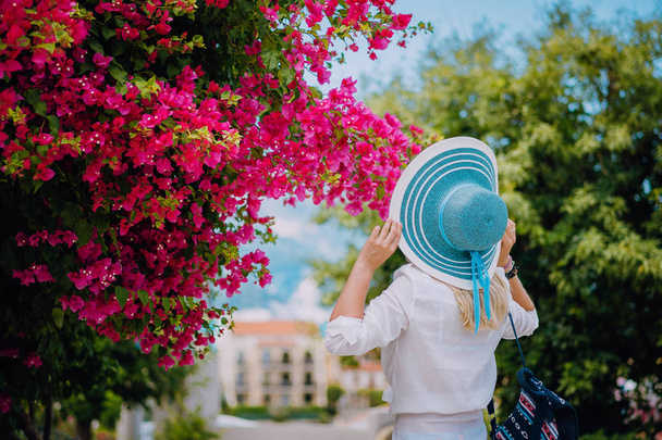Elegant traveler woman with straw hat smelling beautiful colorful flowers on the islands of Greece during summer time. Romantic Traveling vacation concept - Valokuva, kuva