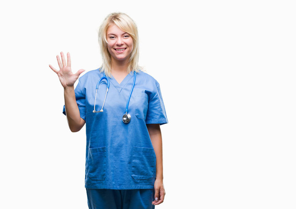 Giovane bella donna medico bionda indossa uniforme medica su sfondo isolato mostrando e indicando con le dita il numero cinque sorridendo fiducioso e felice
. - Foto, immagini