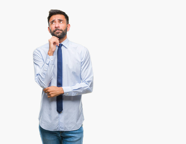 Adult hispanic business man over isolated background with hand on chin thinking about question, pensive expression. Smiling with thoughtful face. Doubt concept. - Фото, изображение