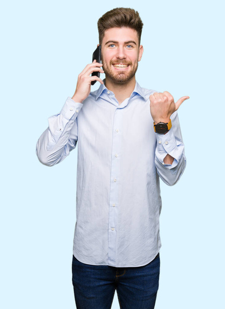 Nuori komea mies liike puhuu älypuhelimella osoittaa ja osoittaa peukalolla sivulle iloinen kasvot hymyillen
 - Valokuva, kuva