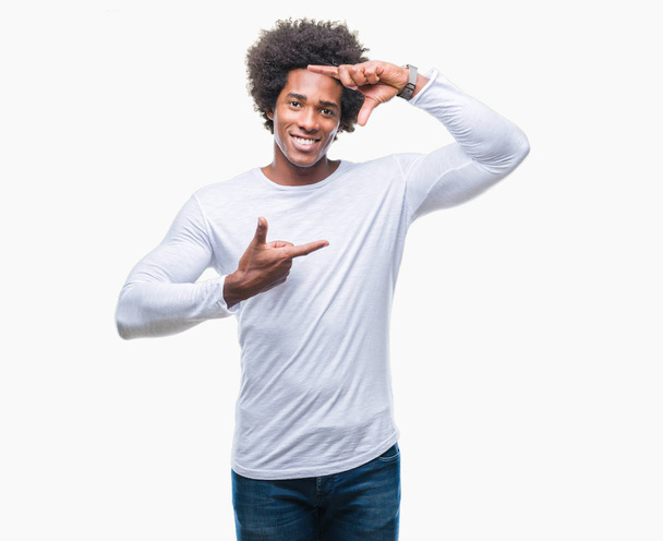 Afro american mężczyzna na białym tle uśmiechający się podejmowania ramki z rąk i palców z szczęśliwy twarz. Koncepcja kreatywność i fotografii. - Zdjęcie, obraz