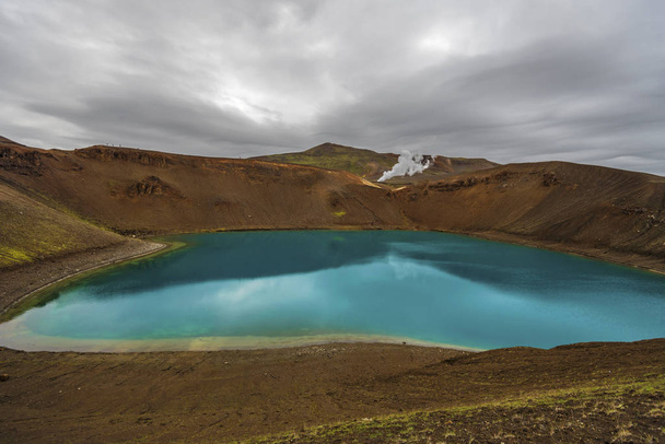 View at Krafla volcanic crater and Viti lake in northern Iceland, vapor of geothermal power plant unit is at background, Nordurland eystra region. - Photo, Image