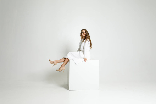 young beautiful girl in white clothes sitting in a white room on a white cube - Foto, Imagem