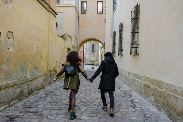 カジュアルなスタイルに身を包んだカップルを愛する若者が冬の旧市街で歩く - 写真・画像