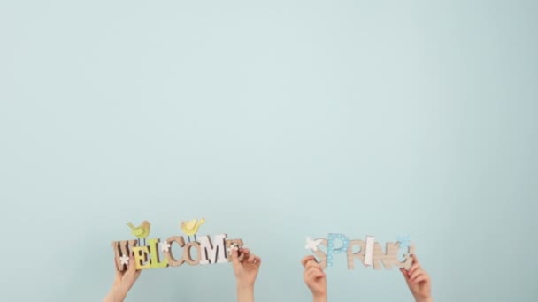 Easter spring decor. Childrens hands are holding and shaking wooden signs with inscriptions Welcome and Spring on a pale blue background in the studio. Copy space at the top of the frame - Filmmaterial, Video