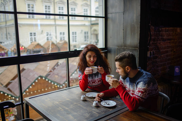 Happy and romantic couple in warm sweaters drink coffee from disposable paper cups in cafeteria. Holidays, christmas, winter, love, hot drinks, people concept - Photo, Image