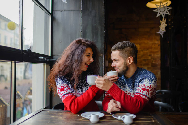 Šťastné a romantický pár v teplé svetry pít kávu z jednorázových papírových kelímků v kavárně. Svátky, Vánoce, zima, láska, teplé nápoje, lidé koncept - Fotografie, Obrázek
