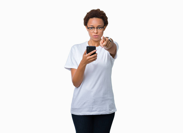Mujer afroamericana joven usando teléfono inteligente sobre fondo aislado apuntando con el dedo a la cámara y a usted, signo de mano, gesto positivo y seguro desde el frente
 - Foto, imagen