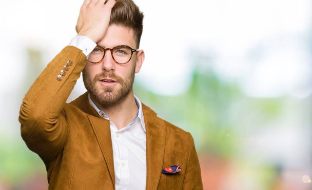Young handsome business man wearing glasses surprised with hand on head for mistake, remember error. Forgot, bad memory concept. - Photo, Image