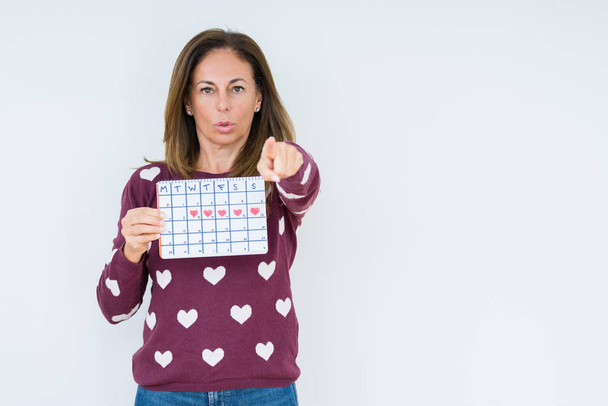 Middle age woman holding menstruation calendar over isolated background pointing with finger to the camera and to you, hand sign, positive and confident gesture from the front - Foto, immagini