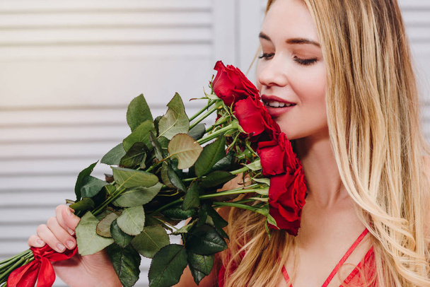 portrait of blonde woman smelling bouquet of red roses, valentines day concept - 写真・画像