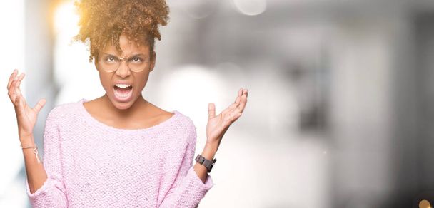 Mooie jonge african american vrouw het dragen van bril geïsoleerd achtergrond gek en gek schreeuwen en schreeuwen met agressieve expressie en wapens aan de orde gesteld. Frustratie concept. - Foto, afbeelding