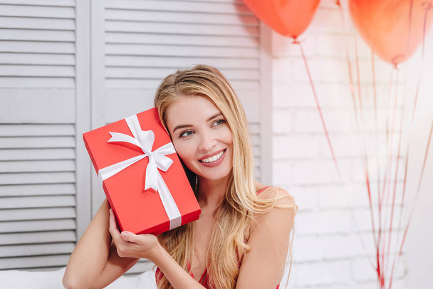 portrait of cheerful woman holding red gift box at the face and looking away, valentines day concept - Φωτογραφία, εικόνα