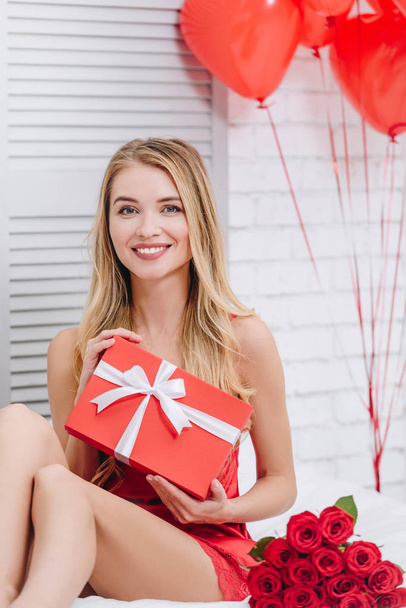 glücklich lächelnde blonde Frau mit Geschenkbox, die in die Kamera schaut, Valentinstag-Konzept - Foto, Bild