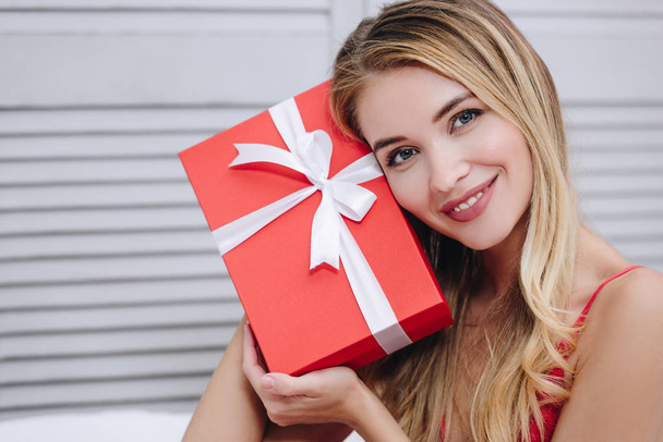 portrait of smiling young woman holding red gift box at the face, valentines day concept - Foto, afbeelding