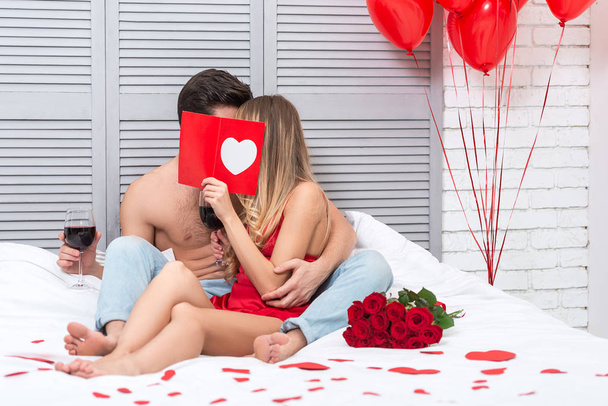 girlfriend and boyfriend kissing behind gift card in the bed at St valentines day - Фото, изображение