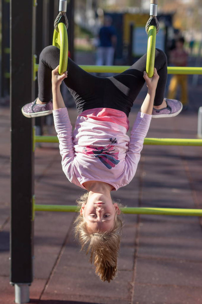 Young girl exercising on gymnastic rings upside down position outside on a playground - Φωτογραφία, εικόνα