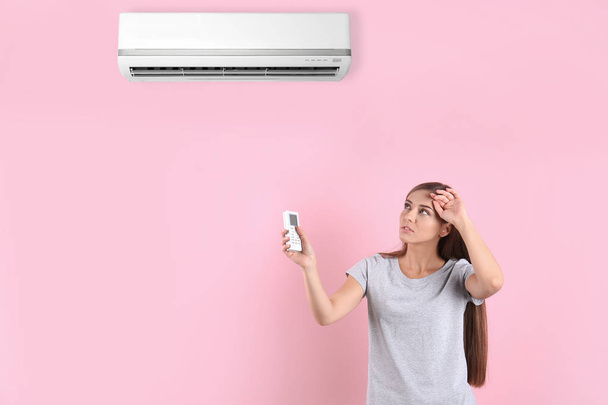 Young woman suffering from heat and turning on air conditioner against color background - Photo, Image