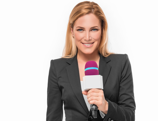 Ελκυστική ξανθιά τηλεόραση παρουσιαστής, κρατώντας ένα μικρόφωνο και σημεία σε ένα αντικείμενο. - Φωτογραφία, εικόνα