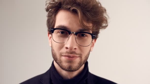 Fashion portrait of handsome elegant man with curly hair wearing suit and glasses on gray background in studio - Footage, Video