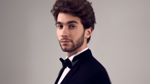 Retrato de moda de hombre elegante guapo con pelo rizado usando esmoquin posando sobre fondo gris en estudio
 - Metraje, vídeo
