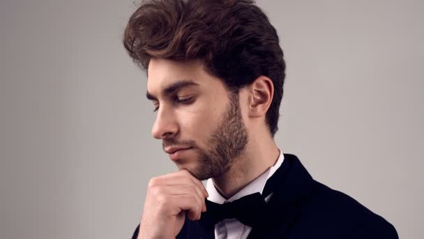 Mode portret van knappe elegante man met krullend haar het dragen van de smoking poseren op grijze achtergrond in de studio - Video
