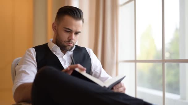 Businessman sitting on armchair and flips through a book. - Metraje, vídeo