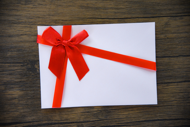 Geschenkkarte auf Holzhintergrund / rosa weiße Geschenkkarte mit roter Schleife dekoriert, um frohe Weihnachten Urlaub frohes neues Jahr oder Valentinstag Geschenkgutschein auf Ton Vintage-Stil Hintergrundansicht - Foto, Bild