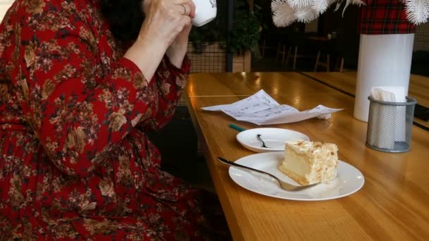 Femme d'affaires boit du café et mange du gâteau dans un café ou un restaurant et écrit des notes sur un morceau de papier
. - Séquence, vidéo