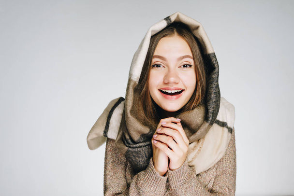 A beautiful young woman wrapped in a scarf is warming her hands and smiling, isolated on white. Winter portrait - Foto, Bild