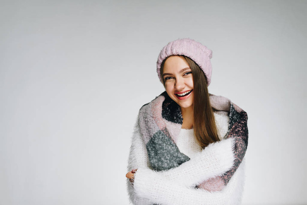 Girl in a warm woolen sweater looks into the camera and laughs, wrapped herself in a scarf, heats up - Fotoğraf, Görsel