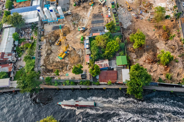 Aerial view of a water bus on a canal in Bangkok, and a construction site along the embankment with heavy equipment preparing for foundation work. - Photo, Image