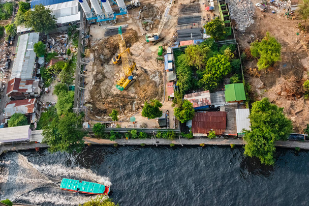 Luchtfoto van een waterbus aan een gracht in Bangkok en een bouwplaats langs de kade met zwaar materieel Funderingswerkzaamheden voorbereiden. - Foto, afbeelding