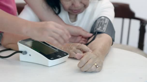 Daughter checking blood pressure (hypertension) of elderly mother at home - Footage, Video