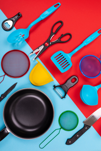 Закрыть портрет сковороды с набором кухонной утвари на красно-синем фоне
 - Фото, изображение
