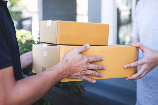 Postbote gibt Paketkasten an Empfänger, junger Besitzer nimmt Pappkartons-Paket von Post, Hauskurier und Lieferservice an. - Foto, Bild