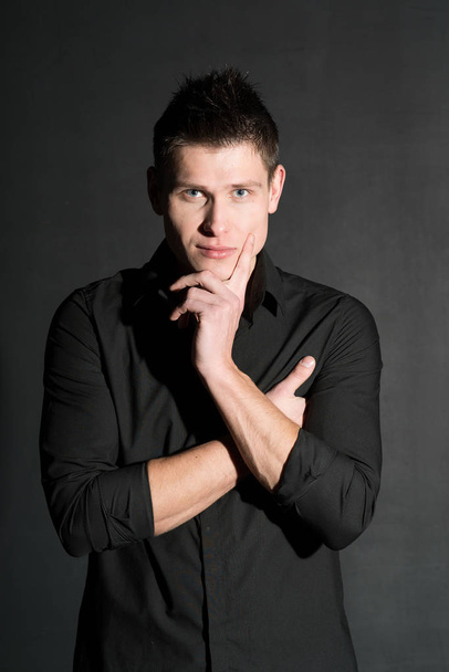 Portrait of young caucasian man in black shirt posing on black background - Photo, Image