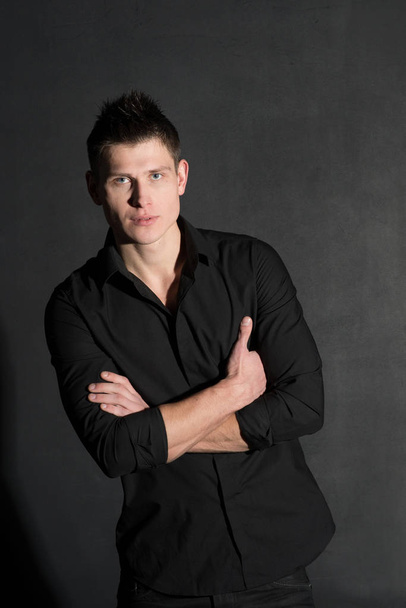 Portrait of young caucasian man in black shirt posing on black background - Foto, afbeelding