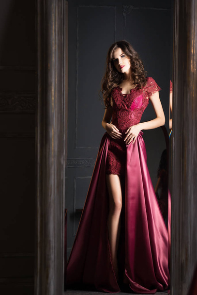 Mirror reflection of young brunette woman in burgundy satin dress - Foto, Imagen