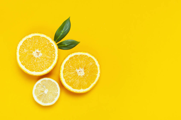 Ripe juicy lemons, orange and green leaves on bright yellow background. Lemon fruit, citrus minimal concept, vitamin C. Creative summer minimalistic background. Flat lay, top view, copy space - Zdjęcie, obraz