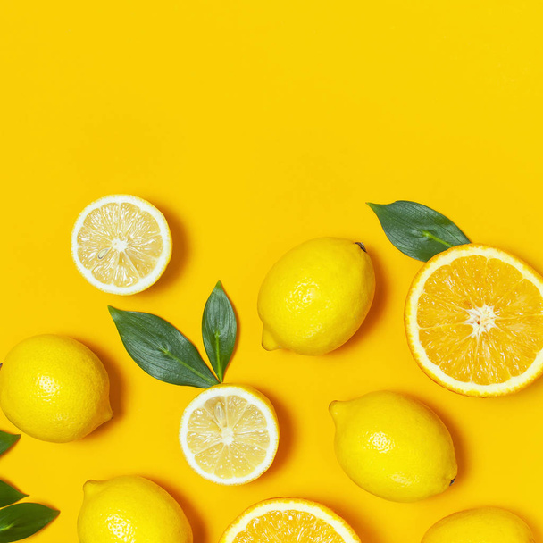 Ripe juicy lemons, orange and green leaves on bright yellow background. Lemon fruit, citrus minimal concept, vitamin C. Creative summer minimalistic background. Flat lay, top view, copy space - Photo, Image